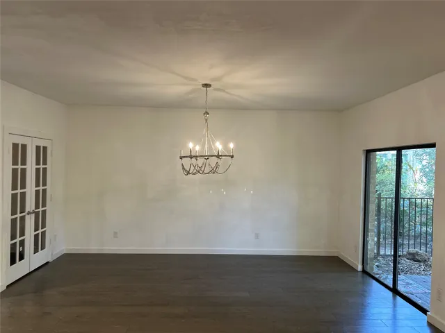 an empty room with wooden floor chandelier and windows