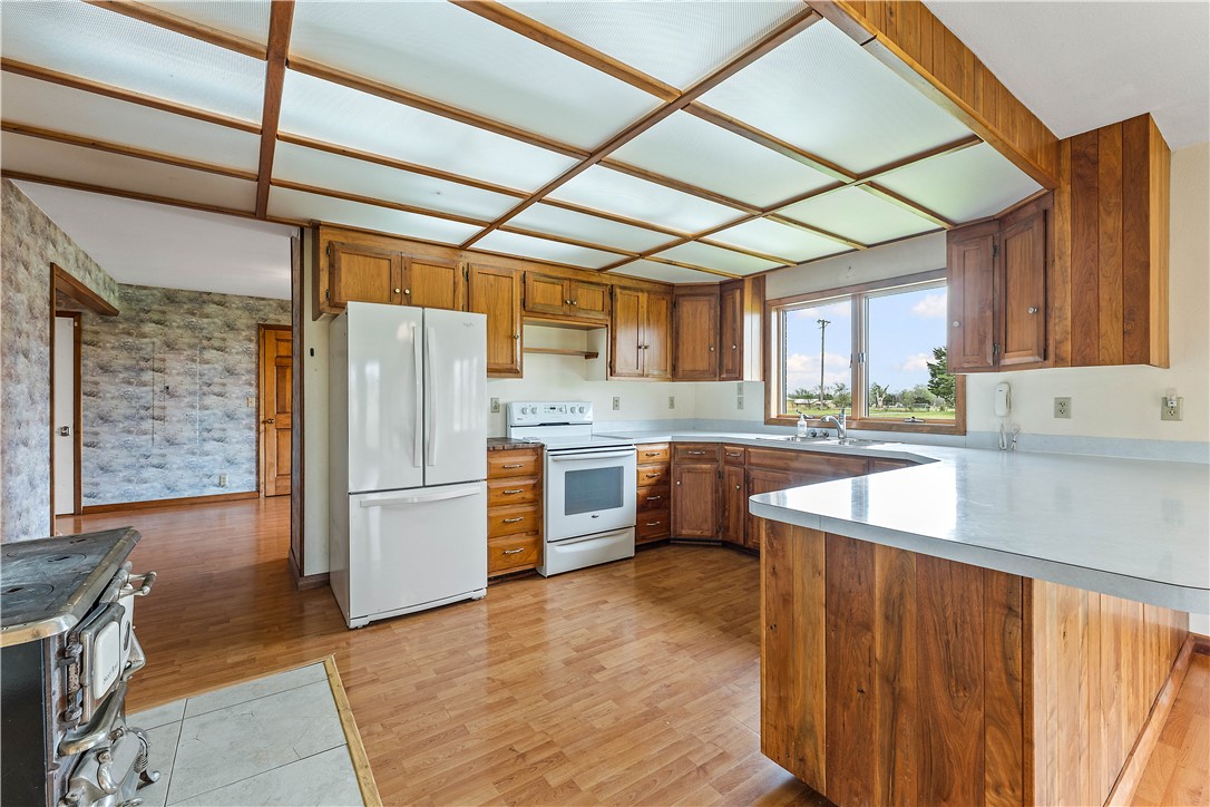 Kitchen with wood finish cabinetry, white appliances, a peninsula, light countertops, and light wood-type flooring