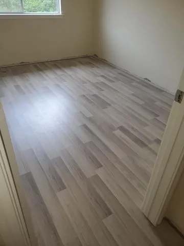 a view of an empty room with wooden floor and window