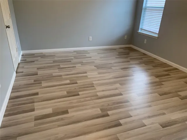 an empty room with wooden floor windows and fan