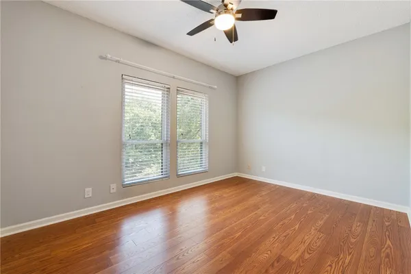 an empty room with wooden floor fan and windows