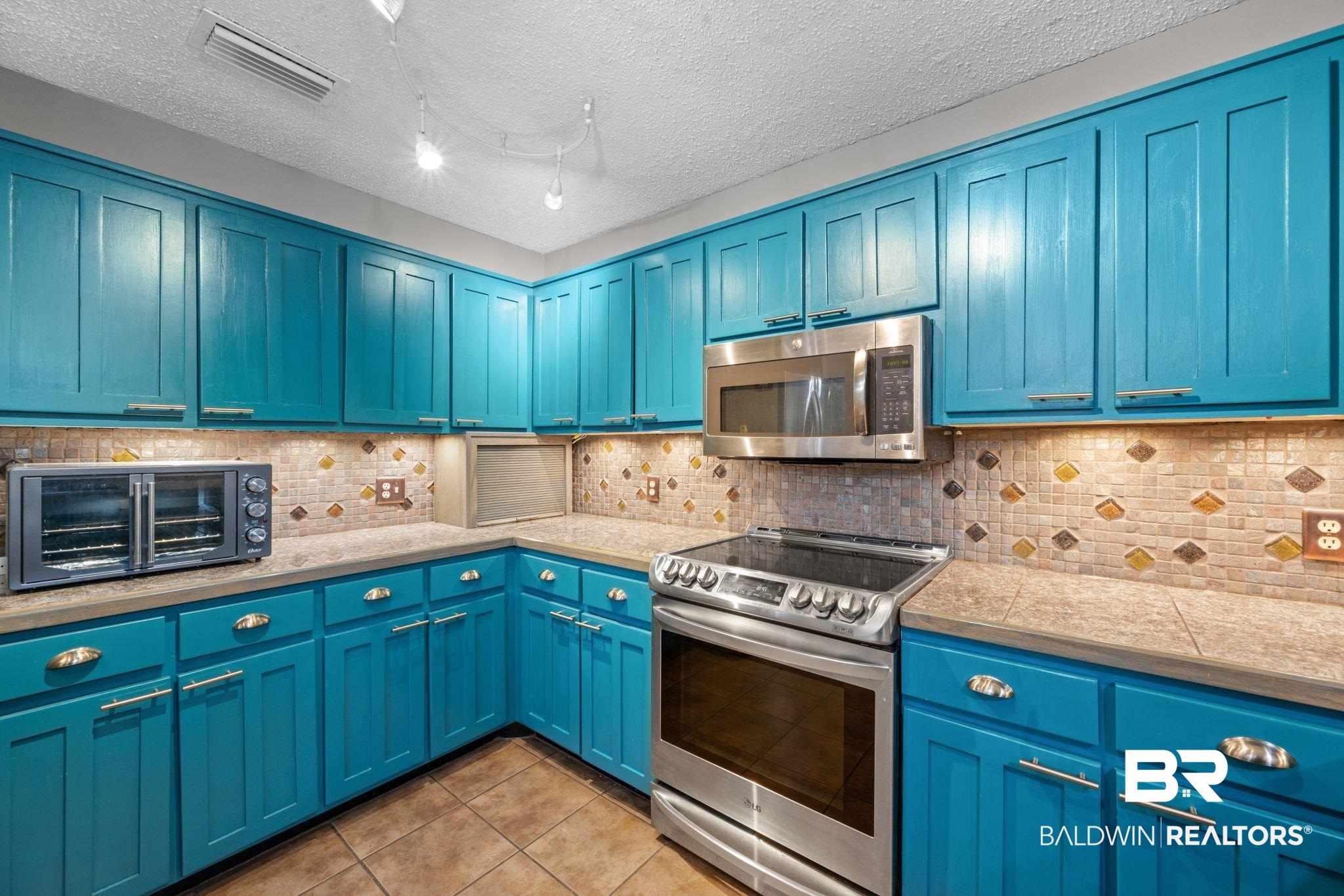 40 Caisson Trace Daphne, AL 36527 - Photo 15 of 54 Kitchen featuring decorative backsplash, appliances with stainless steel finishes, teal cabinets, and light tile patterned floors.