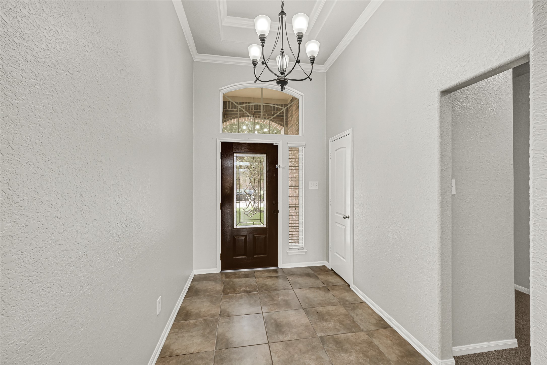 4702 Sedgewood Drive Rosenberg, TX 77471 - Photo 4 of 24 This entryway features a high ceiling with a stylish chandelier, neutral-toned walls, and large tiled flooring. The front door has decorative glass panels, allowing natural light to brighten the space.