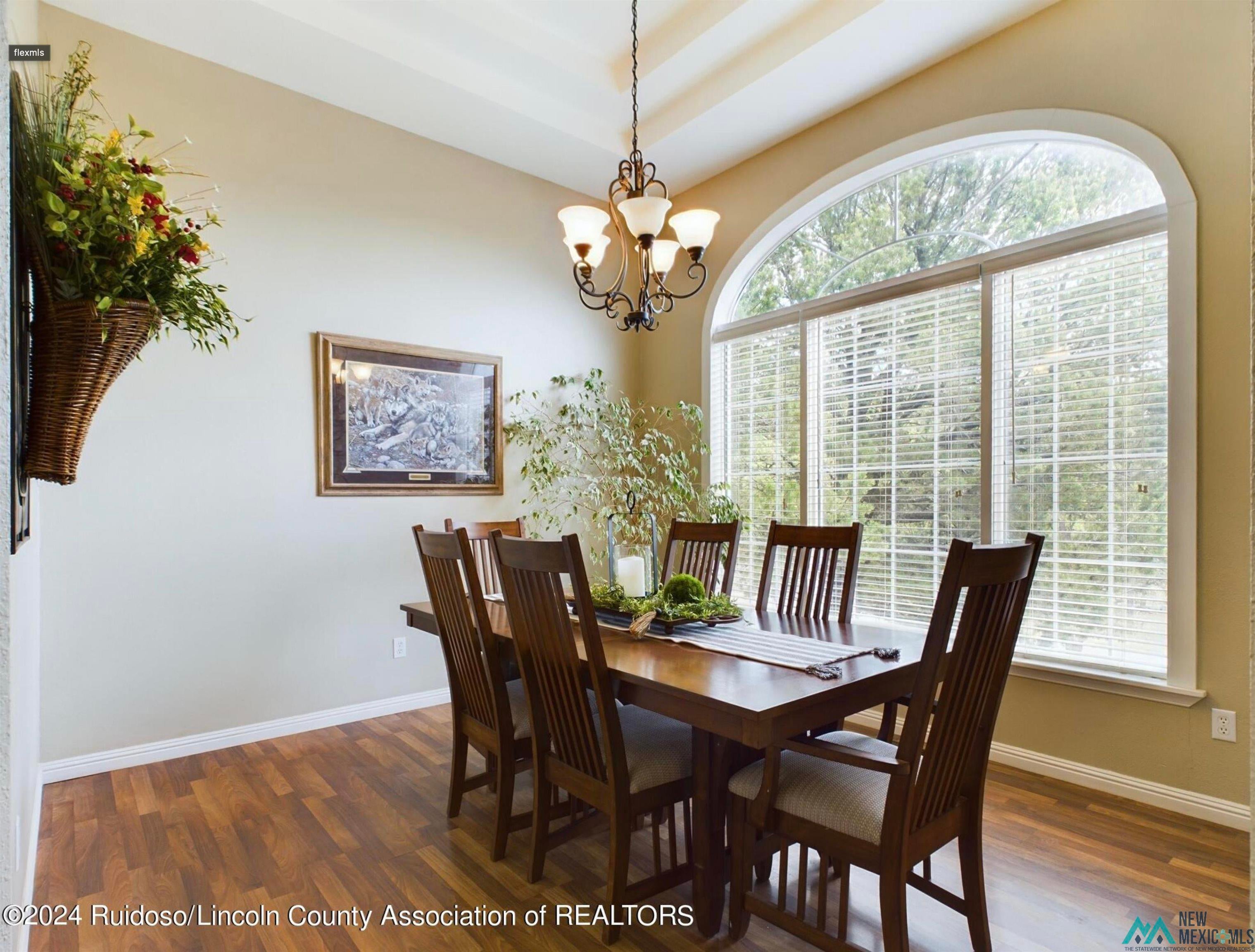 333 Ll Davis Drive Ruidoso, NM 88345 - Photo 9 of 25 Dining area featuring a large arched window with horizontal blinds, wood-finish flooring, a tray ceiling, and an ornate chandelier
