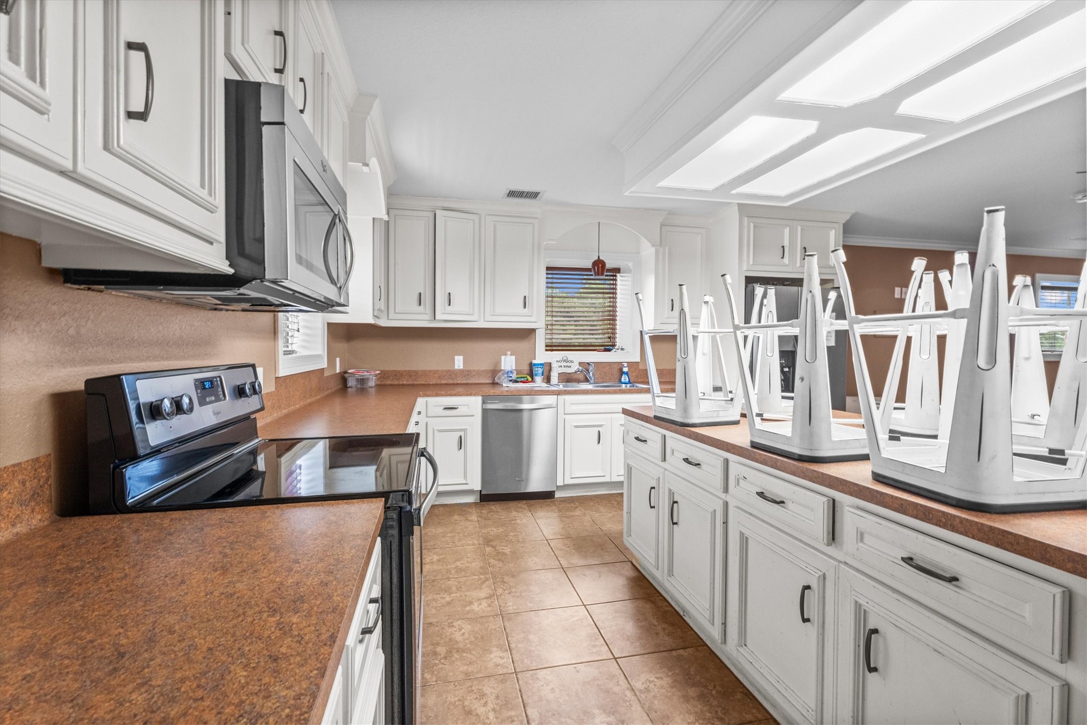 11066 Sh 242 Conroe, TX 77385 - Photo 16 of 21 This spacious kitchen features modern stainless steel appliances, ample white cabinetry, and brown countertops. The room is well-lit with overhead lighting, and there's a large central island with seating space.