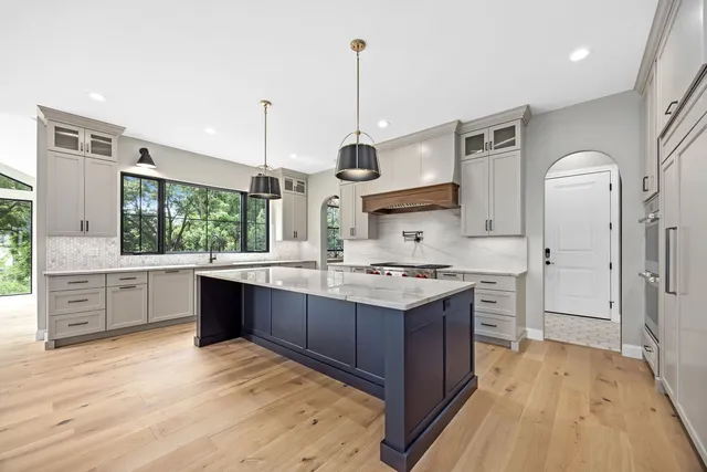 a kitchen with stainless steel appliances granite countertop a stove a sink dishwasher a refrigerator and white cabinets with wooden floor