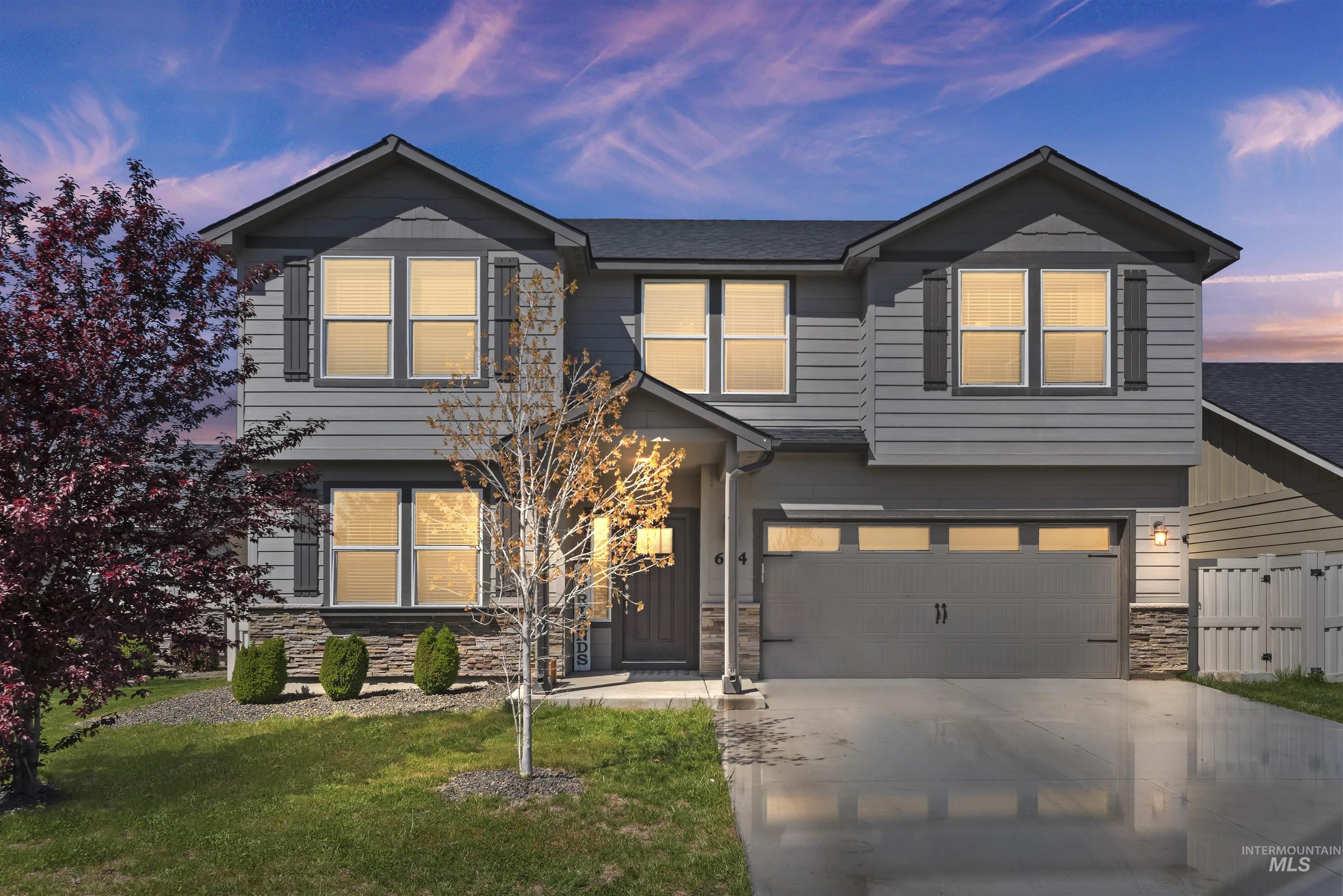 View of front of home with stone, driveway, a two car garage, front lawn, and two trees