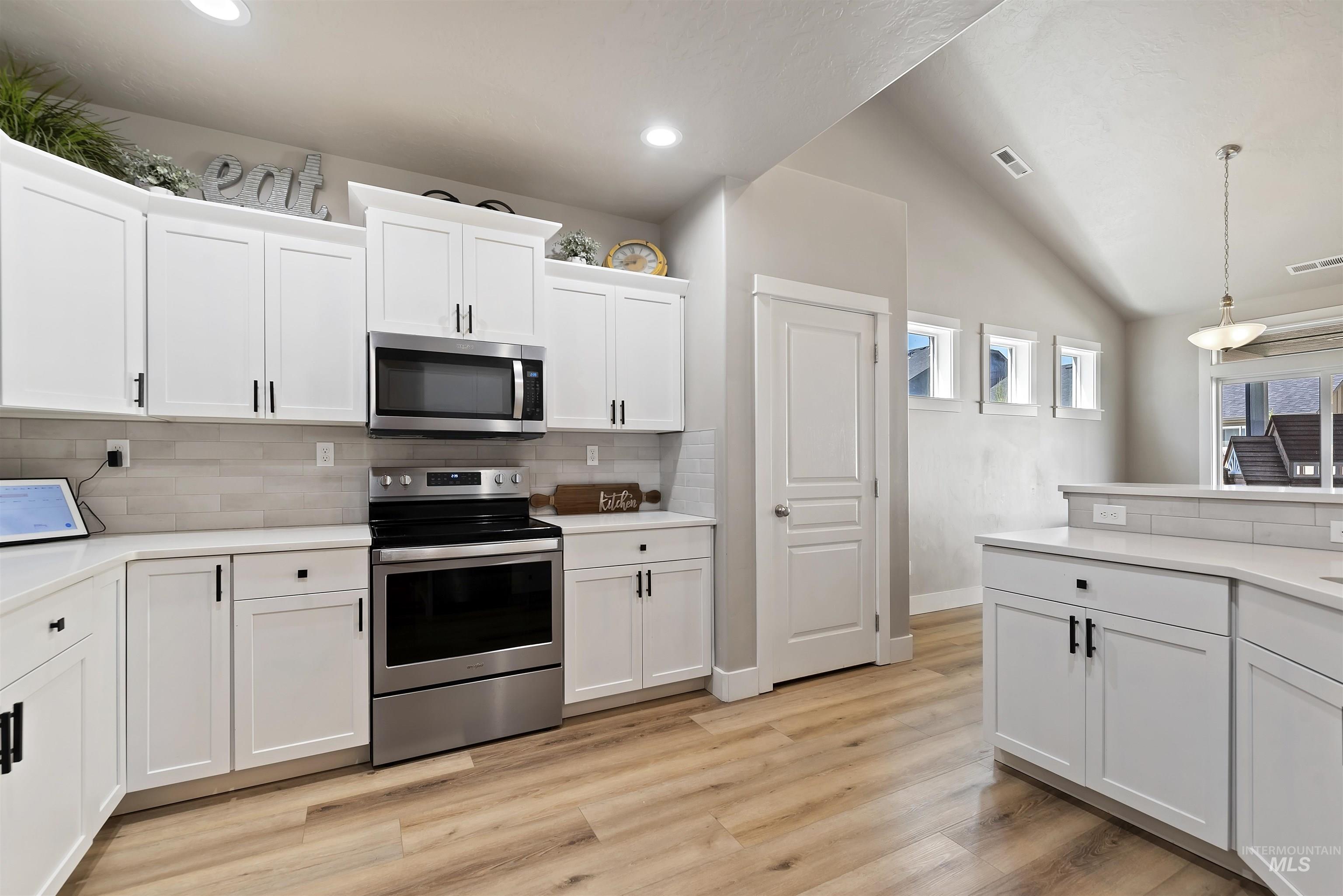 654 Diamond Lake Street Middleton, ID 83644 - Photo 12 of 36 Kitchen featuring stainless steel appliances, white cabinetry, vaulted ceiling, light wood-style floors, and tasteful backsplash