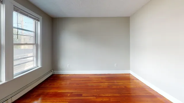 a view of an empty room with wooden floor and a window