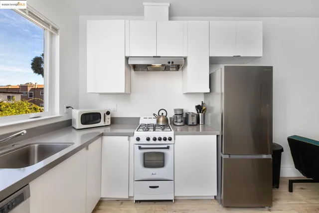 a white kitchen with stainless steel appliances a stove a sink a refrigerator and cabinets