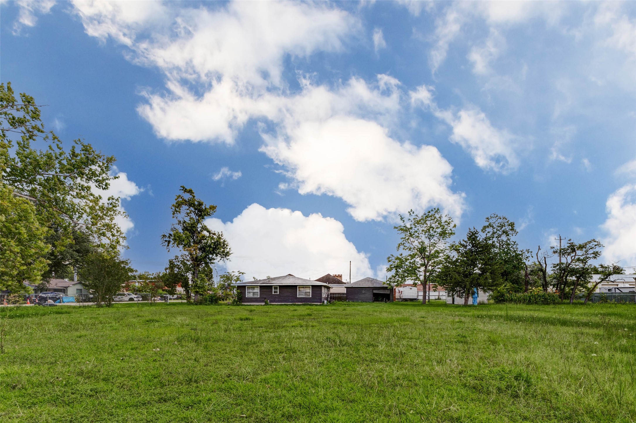 8537 Rannie Road Houston, TX 77080 - Photo 6 of 15 Long rear-lot view showcasing the open field, mature trees, and existing structure positioned beyond the usable land area. The photo highlights the property’s depth, open sightlines, and flexible outdoor footprint. Ideal for buyers focused on land value, this three-parcel lot offers room to evaluate parking, storage, staging, future construction, or redevelopment potential subject to verification.