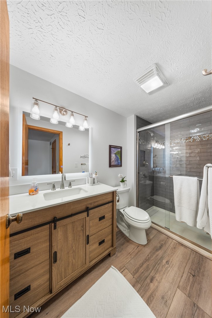 4515 State Road Medina, OH 44256 - Photo 26 of 36 Bathroom with toilet, a textured ceiling, wood finished floors, a shower stall, and vanity