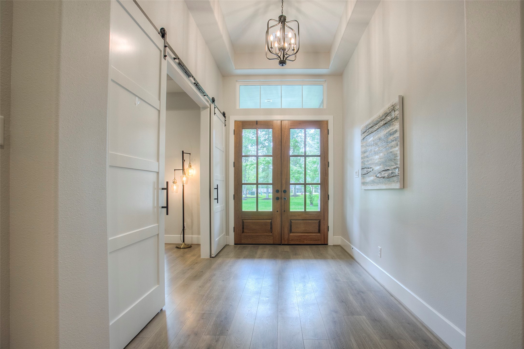 12915 Oak Barrel Road Willis, TX 77378 - Photo 4 of 46 This welcoming entryway features double wooden doors with glass panels, high ceilings, a modern chandelier, and light wood flooring. A barn-style sliding door and contemporary artwork add style and functionality. Natural light enhances the bright, airy ambiance.
