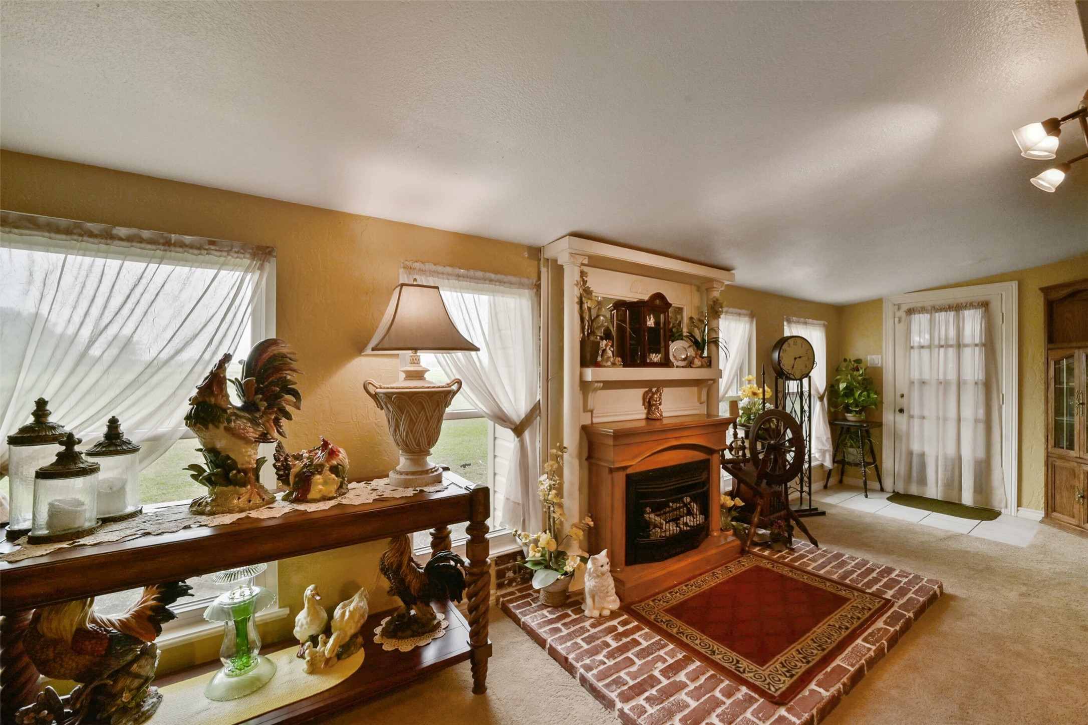 13710 Mueck Road Needville, TX 77461 - Photo 12 of 42 Discover a cozy living room with a charming fireplace, abundant natural light from large windows, and seamless access to outdoor space through elegant glass doors.