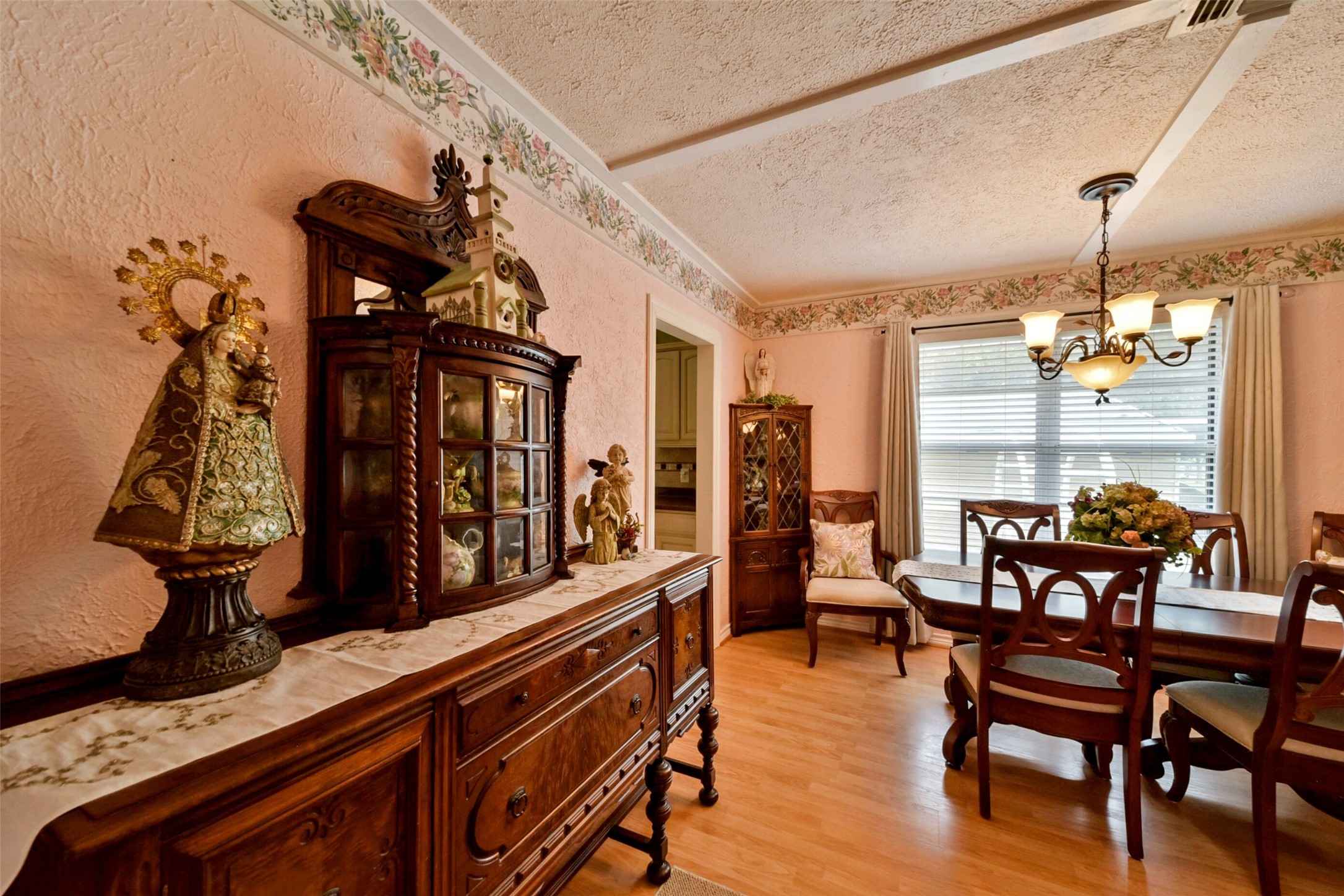 13710 Mueck Road Needville, TX 77461 - Photo 21 of 42 This is a traditional dining room featuring an elegant wood dining set, a matching buffet with a marble top, and a classic chandelier. The room is well-lit by natural light from a large window with blinds, and is decorated with floral wallpaper borders and decorative items. A cozy and inviting space for family meals and gatherings.
