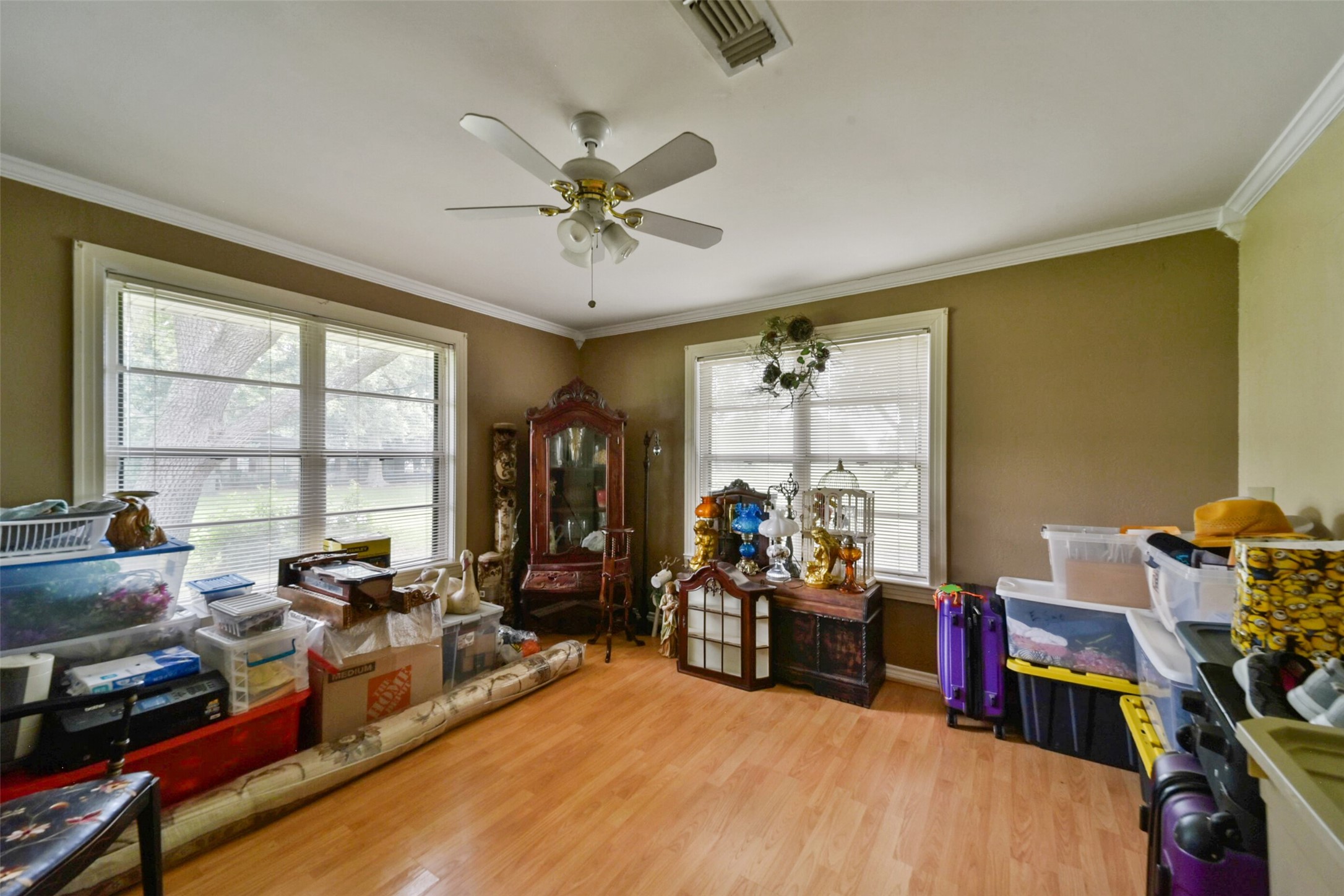 13710 Mueck Road Needville, TX 77461 - Photo 22 of 42 The room features hardwood flooring, a ceiling fan, and ample natural light from three large windows. The walls are painted in neutral tones. Currently, the space is cluttered with personal belongings, indicating it is used for storage.