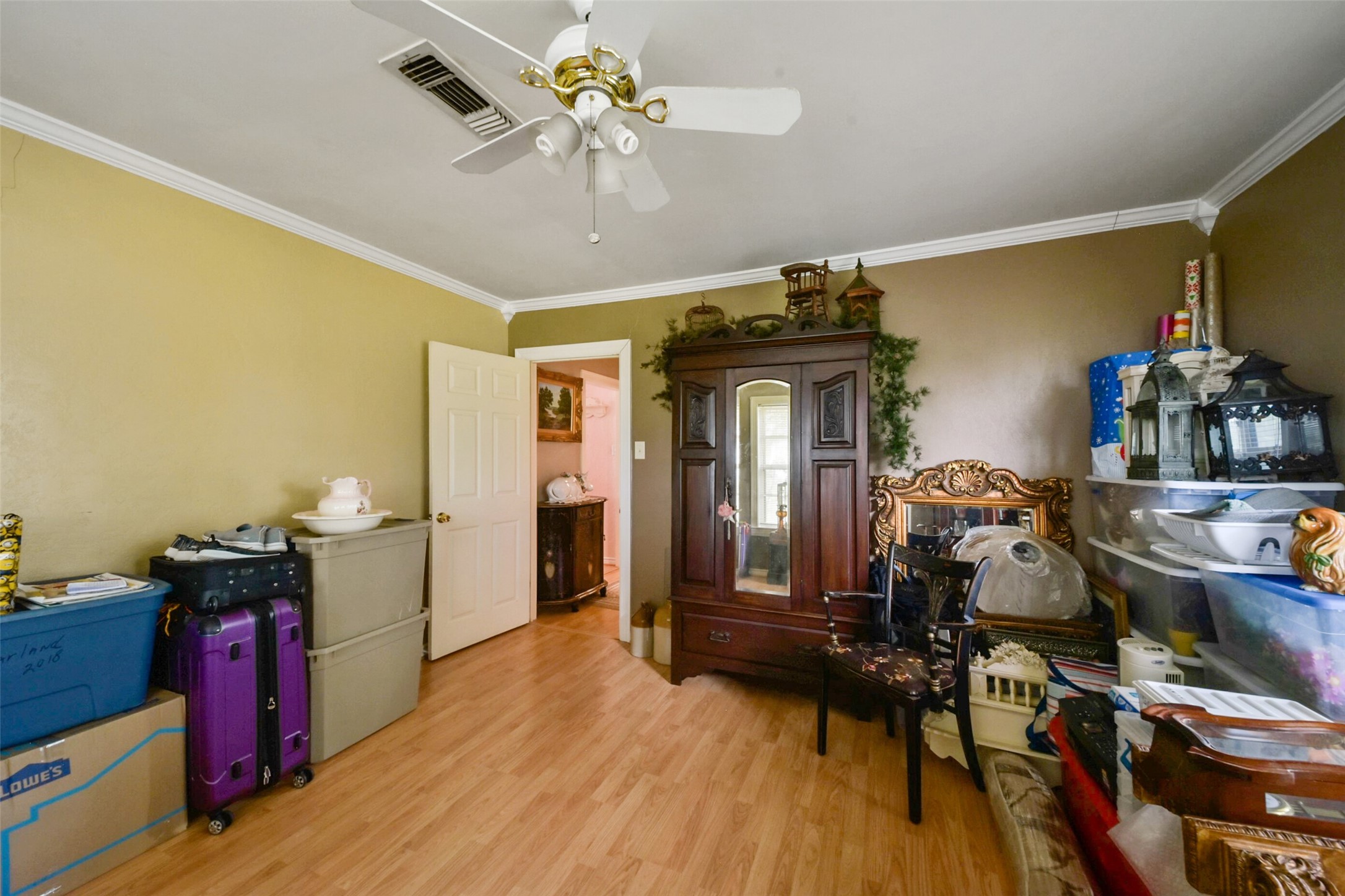 13710 Mueck Road Needville, TX 77461 - Photo 23 of 42 This is a spacious room featuring hardwood floors, a ceiling fan, and a mix of neutral and warm wall colors. It is currently furnished and contains personal belongings, indicating it is lived-in. There is an ornate wooden furniture piece and a doorway leading to an adjacent room.