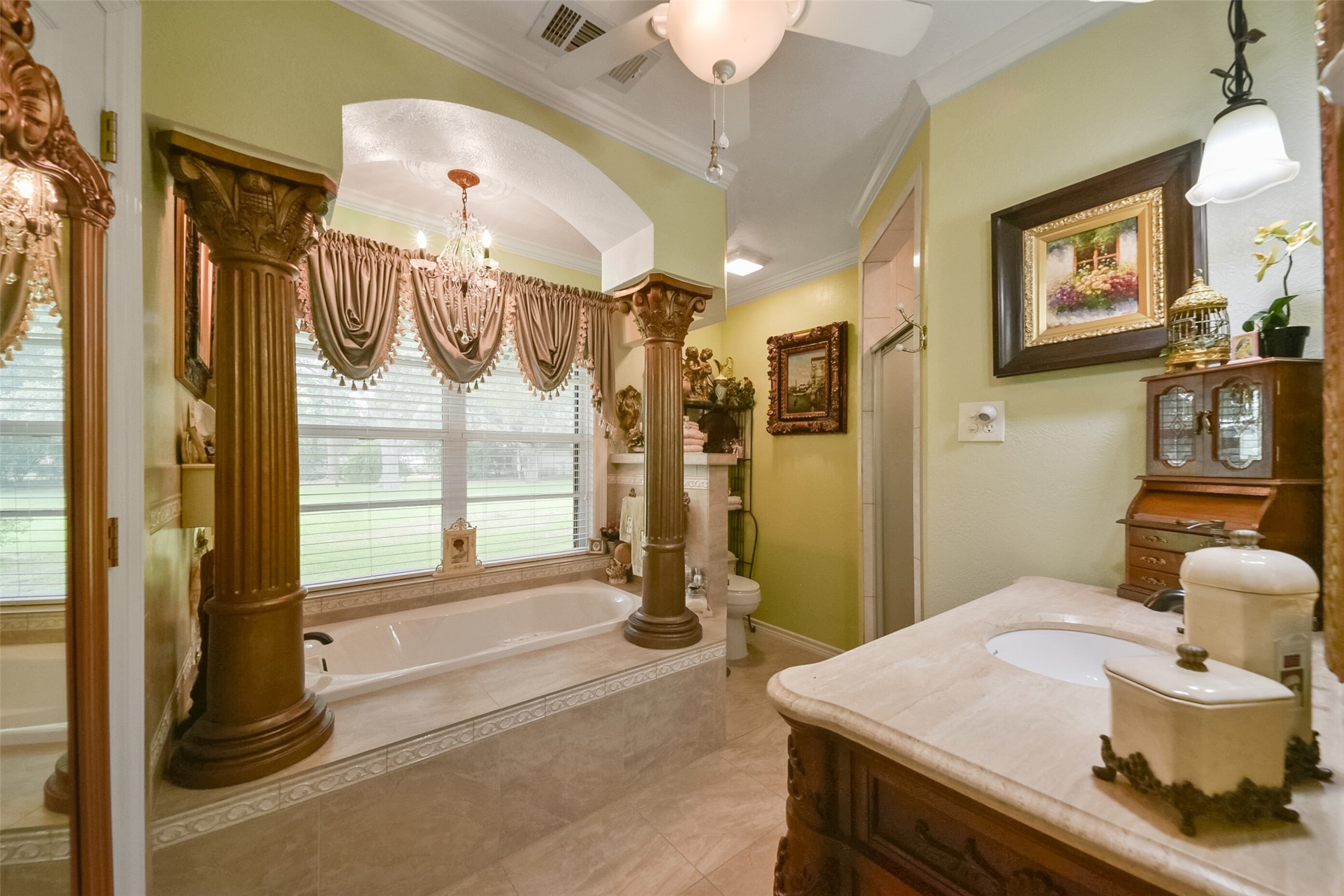 13710 Mueck Road Needville, TX 77461 - Photo 29 of 42 This is an elegantly appointed bathroom featuring a large soaking tub with window views, ornate columns, a chandelier, and a separate shower and vanity area.