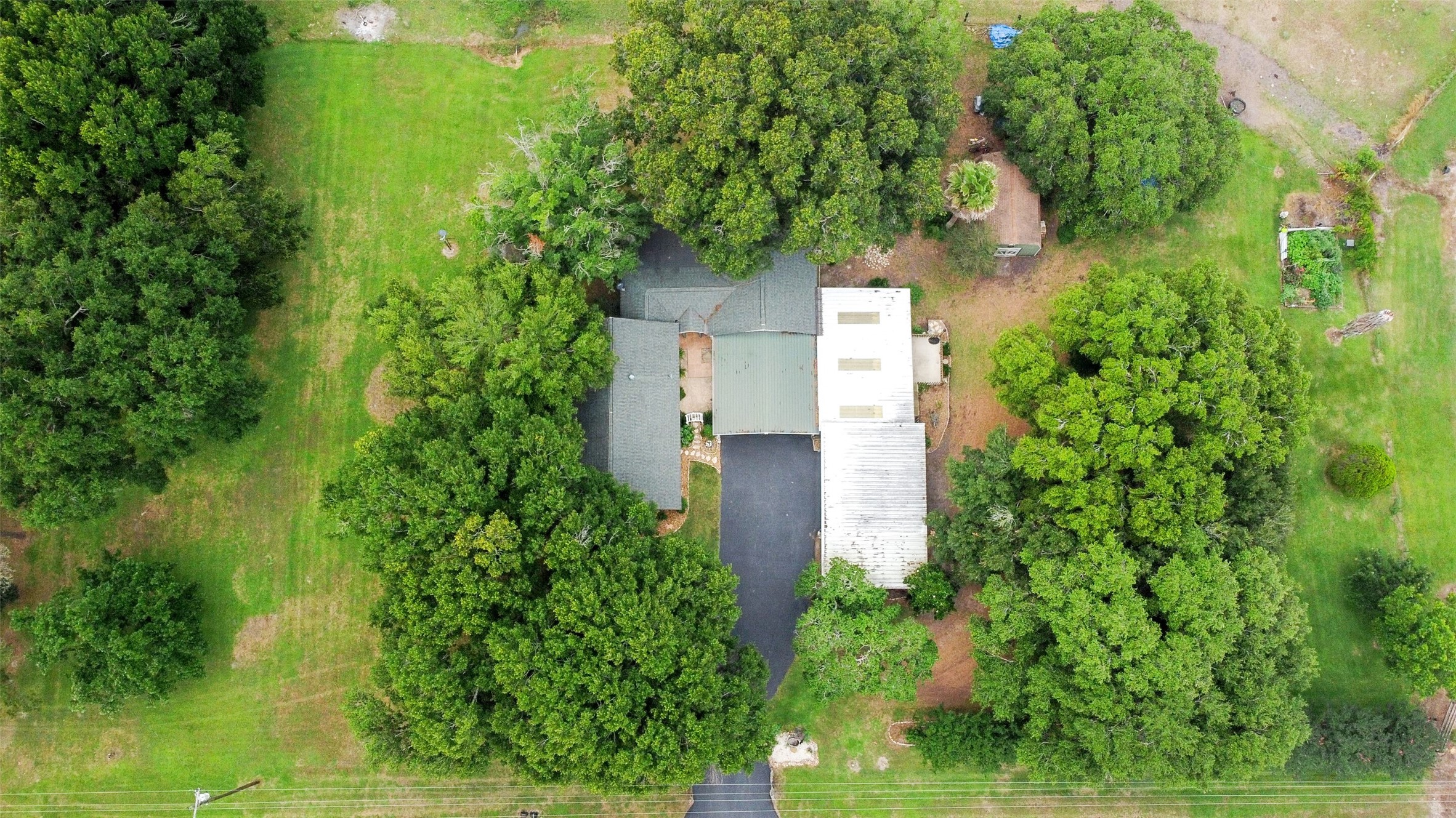 13710 Mueck Road Needville, TX 77461 - Photo 3 of 42 This aerial view showcases a secluded property nestled in lush greenery, featuring a spacious home with multiple roofs and an adjacent garage or workshop, offering ultimate privacy and a serene connection with nature.