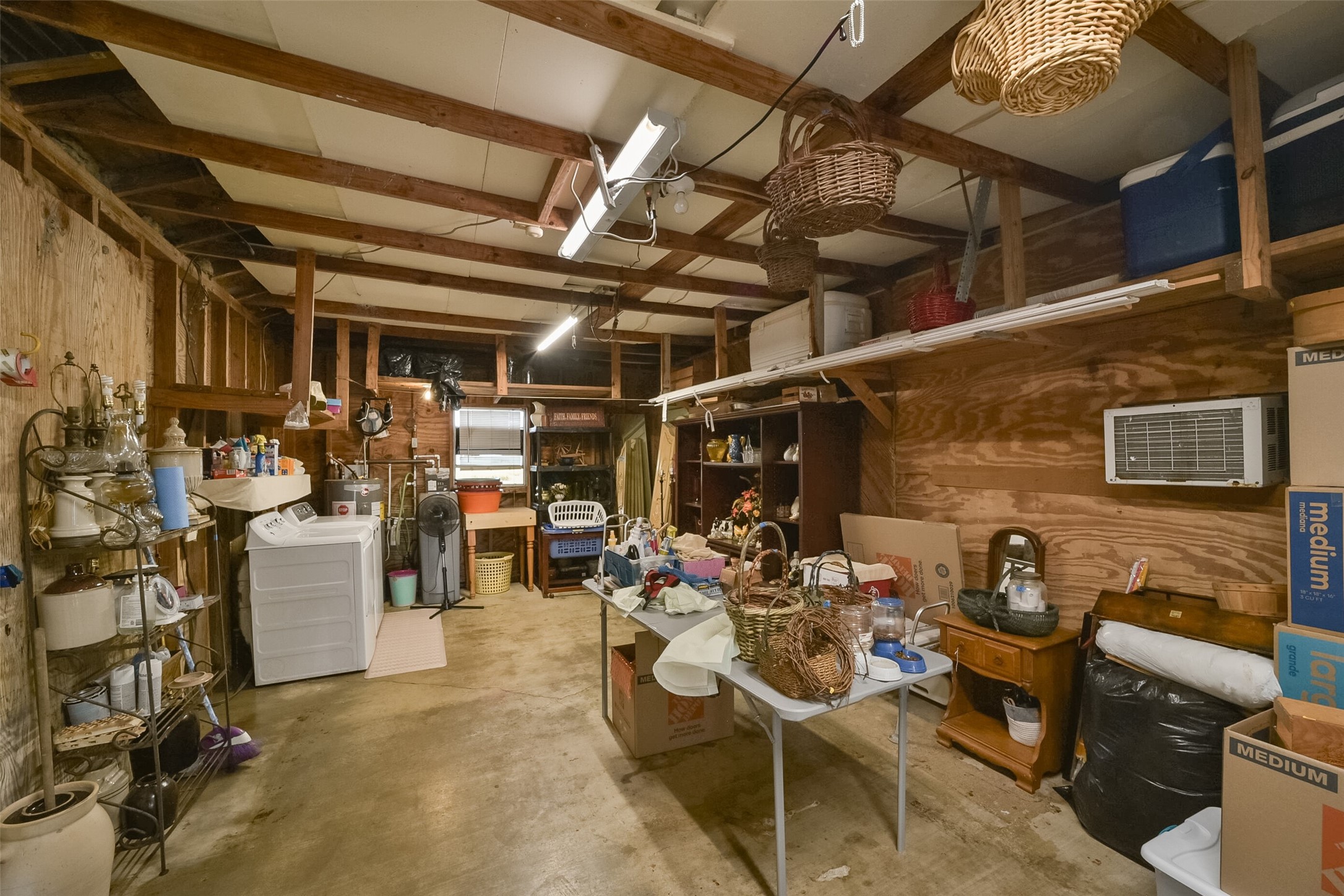 13710 Mueck Road Needville, TX 77461 - Photo 32 of 42 This is a spacious, unfinished basement with exposed wooden beams and ample storage space. It includes a laundry area with a washer and dryer, shelving units, and is well-lit with multiple ceiling fixtures.