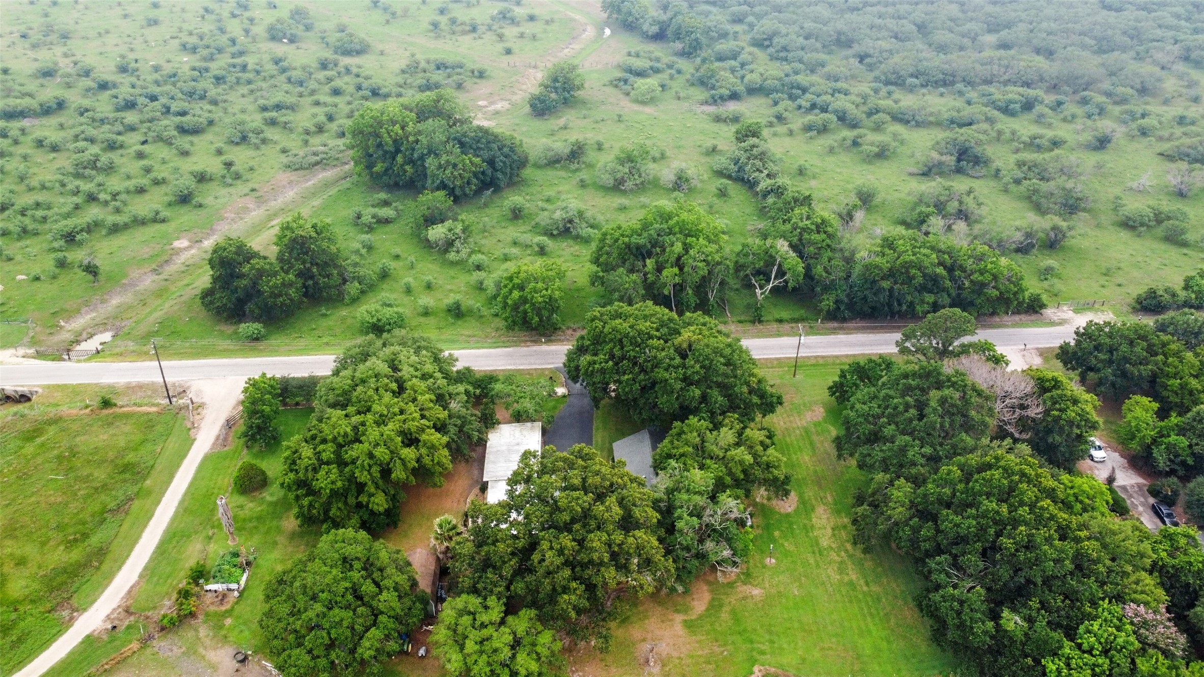 13710 Mueck Road Needville, TX 77461 - Photo 7 of 42 This aerial view showcases a serene rural property with expansive green spaces, mature trees, and open fields, all accessible via a paved road. Ideal for privacy and tranquility.