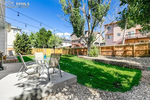 a view of a backyard with table and chairs potted plants and large tree