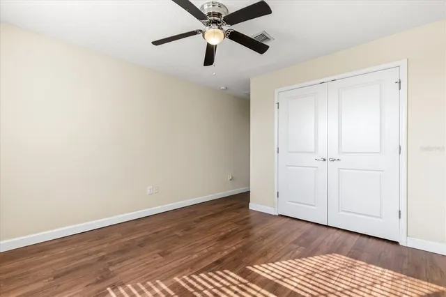 an empty room with wooden floor ceiling fan and windows