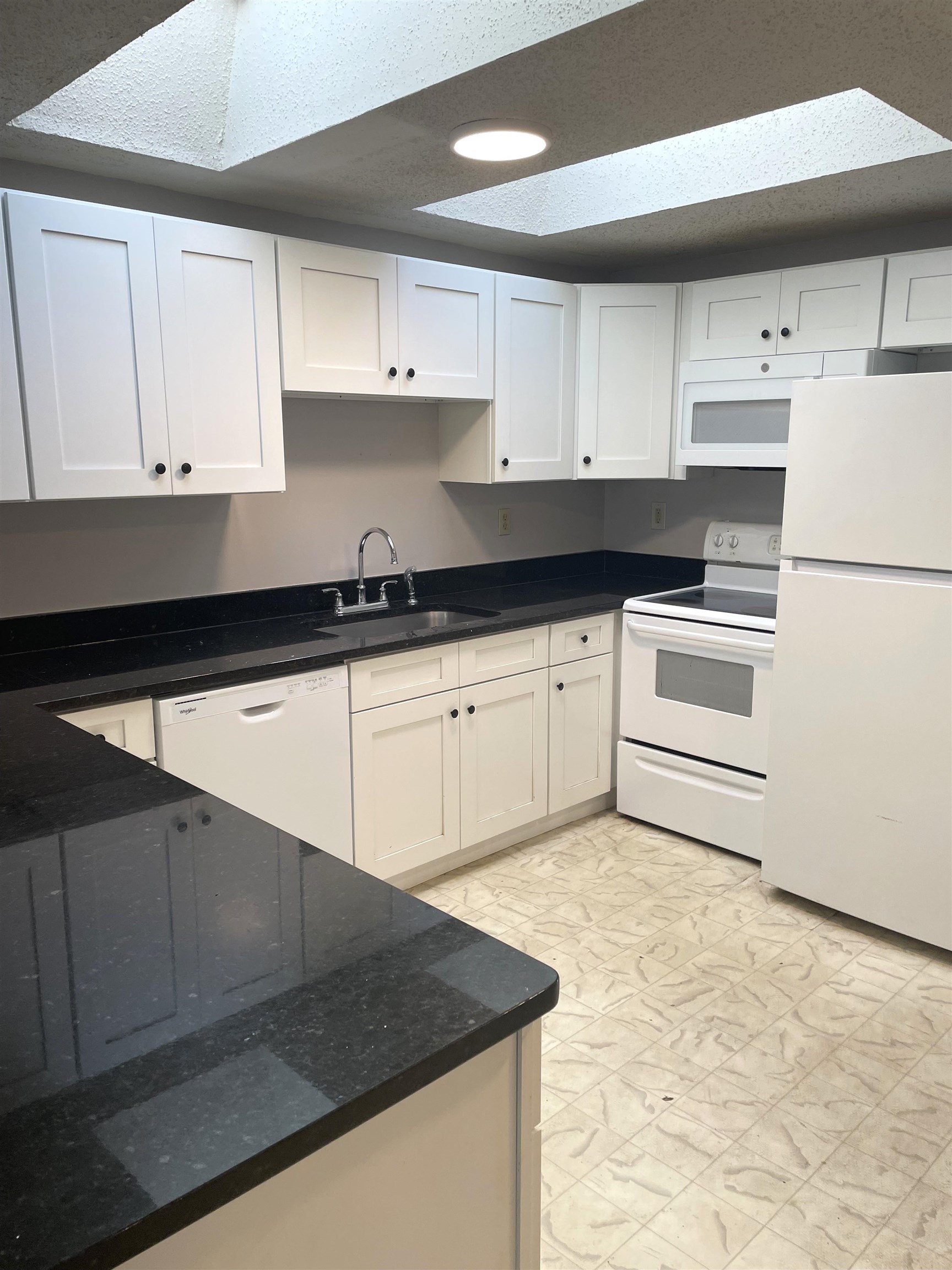 137.5 Riberia Street St. Augustine, FL 32084 - Photo 3 of 10 Kitchen featuring white appliances, white cabinetry, dark stone counters, light floors, and a skylight