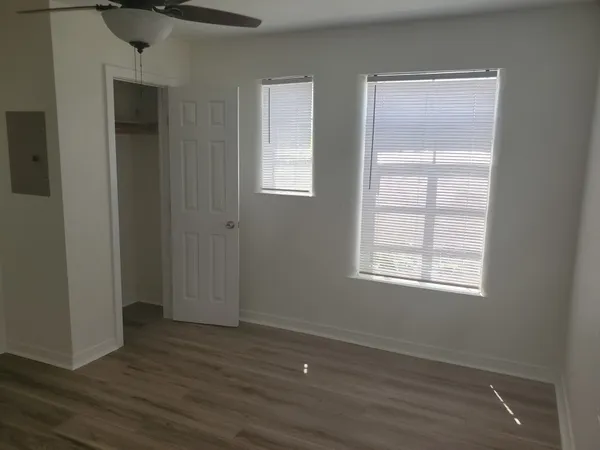 an empty room with wooden floor closet and windows