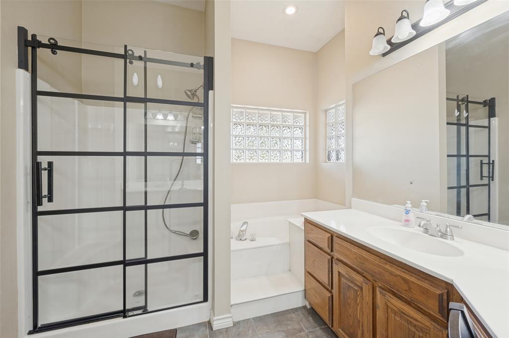 1601 East Blackjack Road East Pilot Point, TX 76258 - Photo 13 of 30 Glass-enclosed shower with black grid accents, built-in bathtub, glass block windows, wood-finish vanity with countertop, and a large wall-mounted mirror