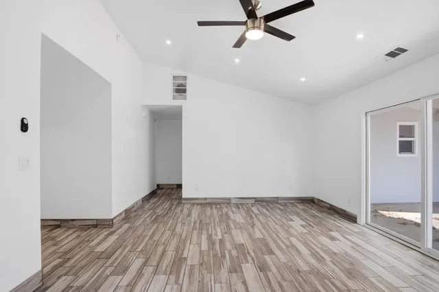 an empty room with wooden floor a ceiling fan and windows