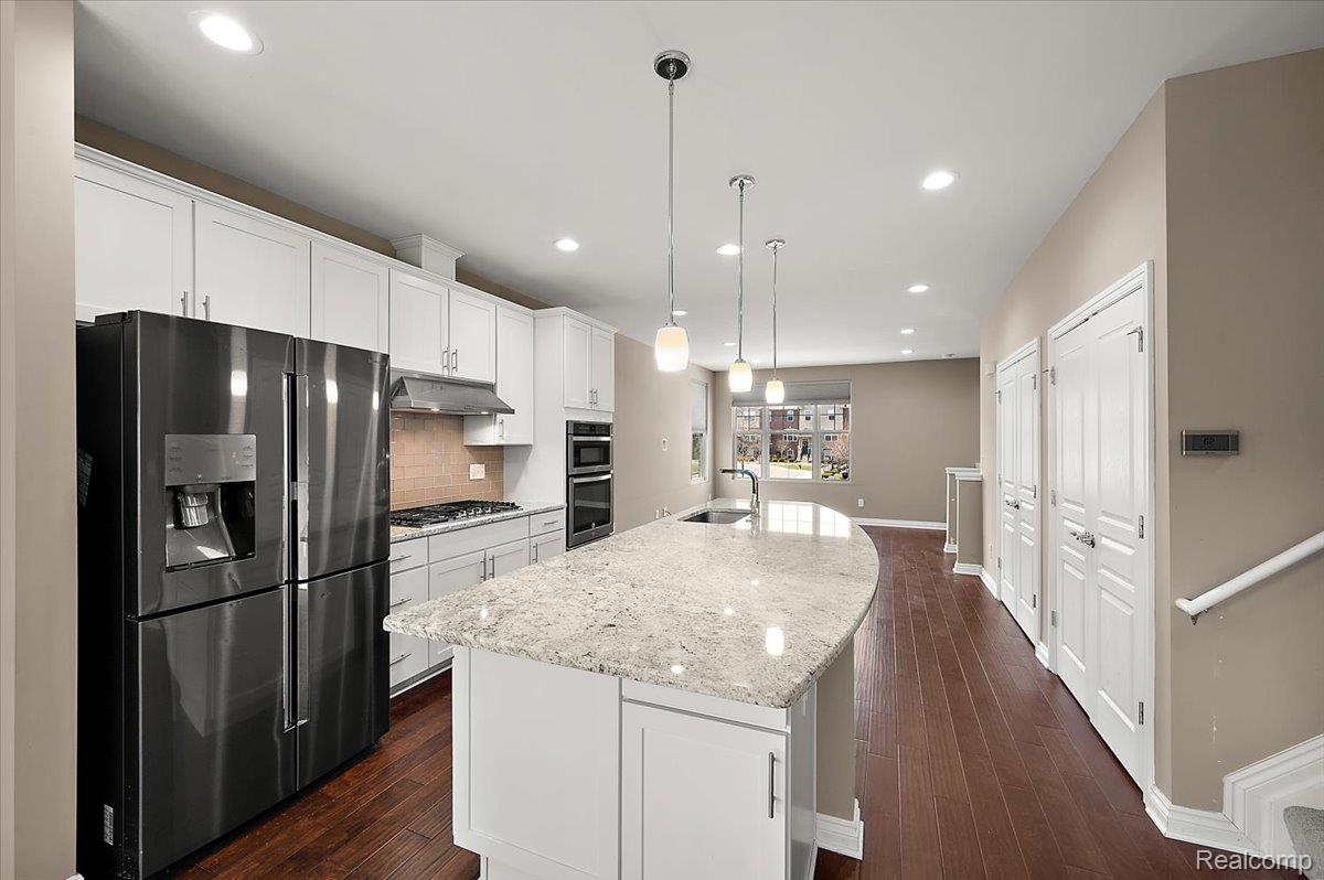 2877 Hartwick Drive Rochester, MI 48307 - Photo 20 of 44 Kitchen featuring stainless steel appliances, a kitchen island with sink, white cabinetry, backsplash, and light stone countertops