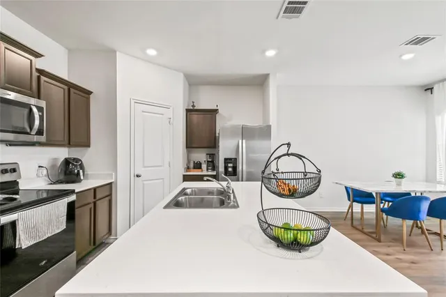 a kitchen with stainless steel appliances a sink a stove a refrigerator cabinets and dining table