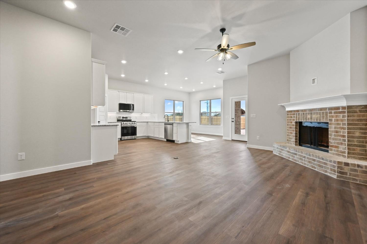 13604 Wheeler Avenue Lubbock, TX 79423 - Photo 3 of 23 an empty room with wooden floor fireplace and kitchen view