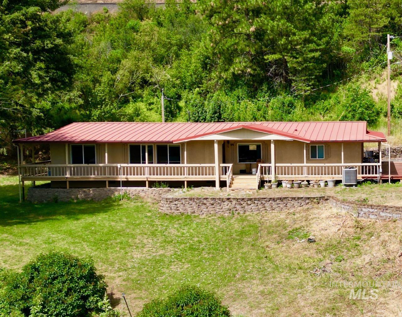 35322 River Road Lenore, ID 83541 - Photo 2 of 42 Ranch-style residence featuring a metal roof, an expansive front porch with wood railings, multiple windows, and a surrounding natural landscape