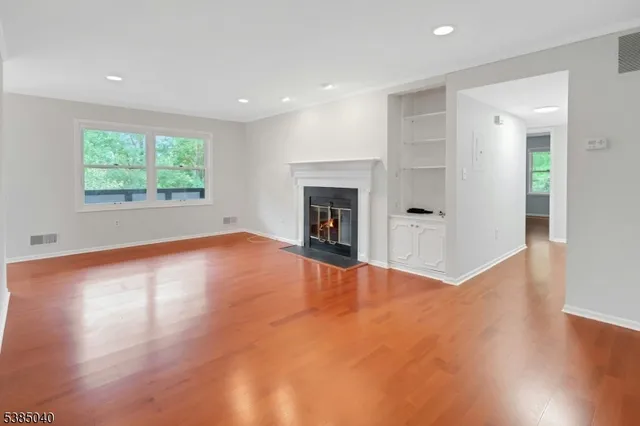 an empty room with wooden floor fireplace and windows