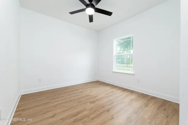 an empty room with wooden floor ceiling fan and windows
