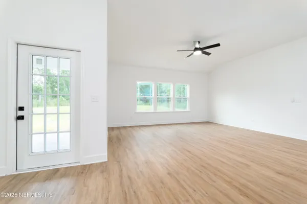 an empty room with wooden floor ceiling fan and windows