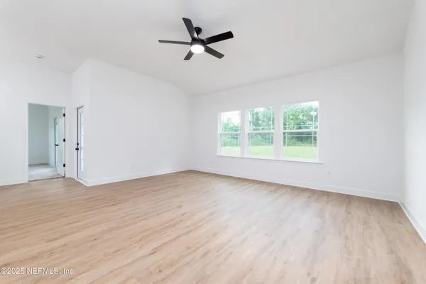 an empty room with wooden floor ceiling fan and windows