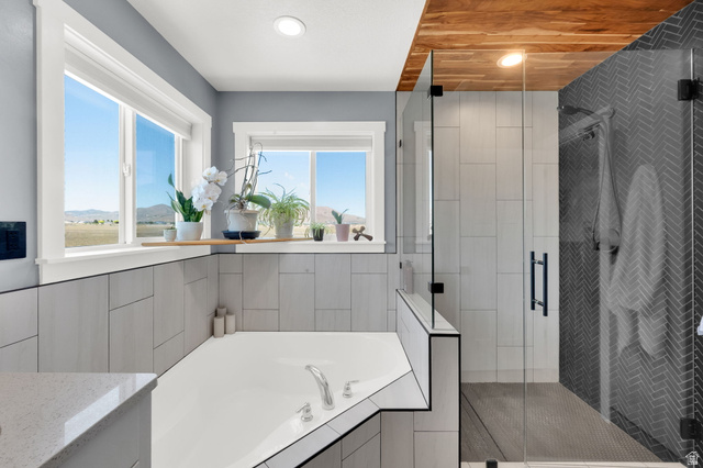 1857 Thunder Gulch Road Eagle Mountain, UT 84005 - Photo 23 of 50 Freestanding soaking tub with integrated deck, surrounded by large windows, glass-enclosed shower with herringbone tile, and wood-paneled ceiling accent