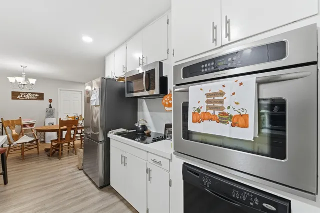 a kitchen with stainless steel appliances kitchen island granite countertop a stove top oven a sink a dining table and chairs with wooden floor