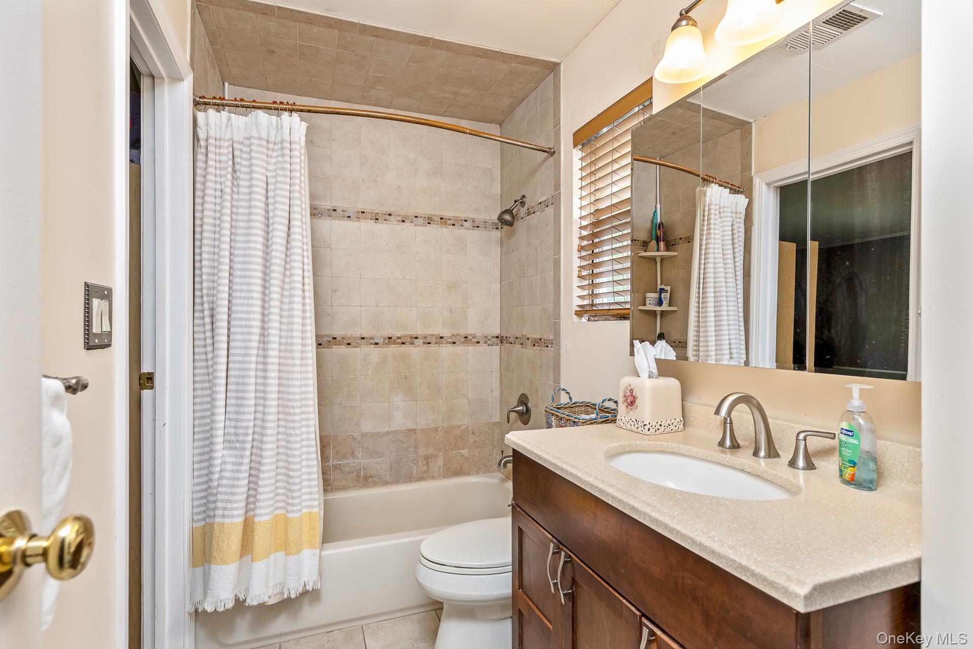 17 Stone Commons Yaphank, NY 11980 - Photo 21 of 31 Bathroom featuring a wood-finish vanity with a light-toned countertop, a shower-over-tub combination with tiled surround, and a wall-mounted mirror above the vanity
