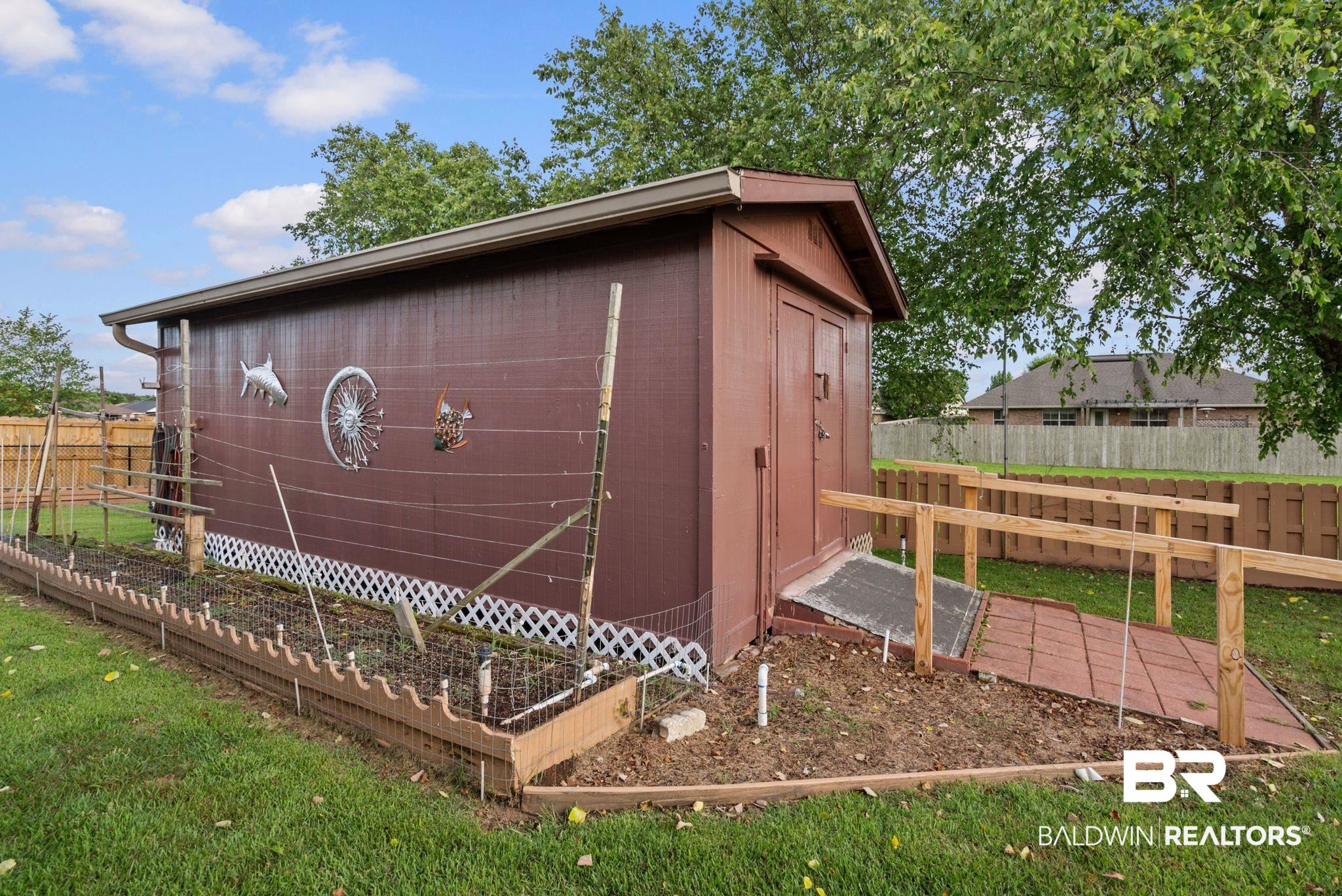 562 Vestige Mews Foley, AL 36535 - Photo 42 of 54 Brown storage shed with a coordinating access ramp, featuring a garden bed with lattice skirting, and a perimeter fence
