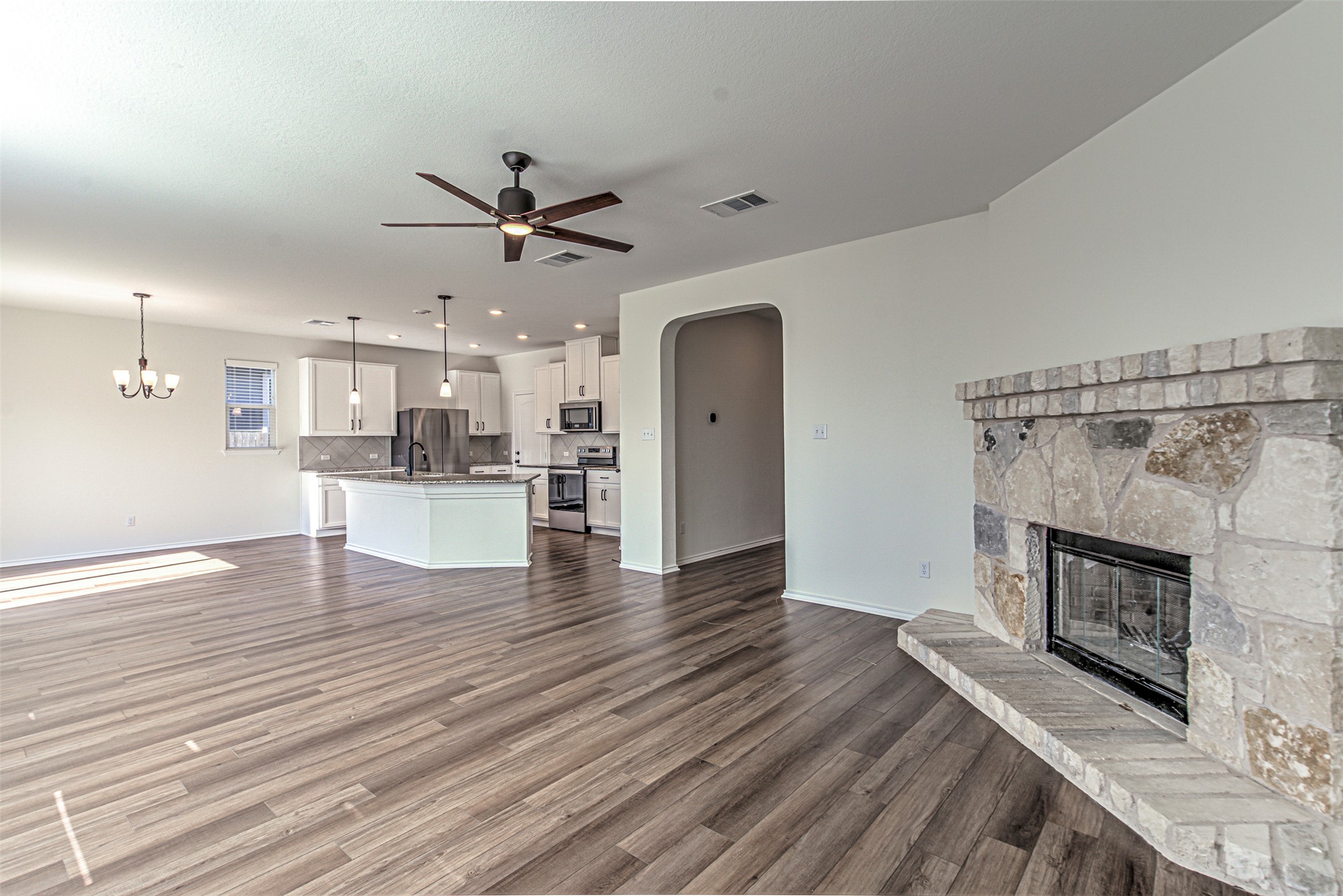 486 Gustaf Trail Kyle, TX 78640 - Photo 5 of 40 a view of a kitchen and an empty room with wooden floor a fireplace