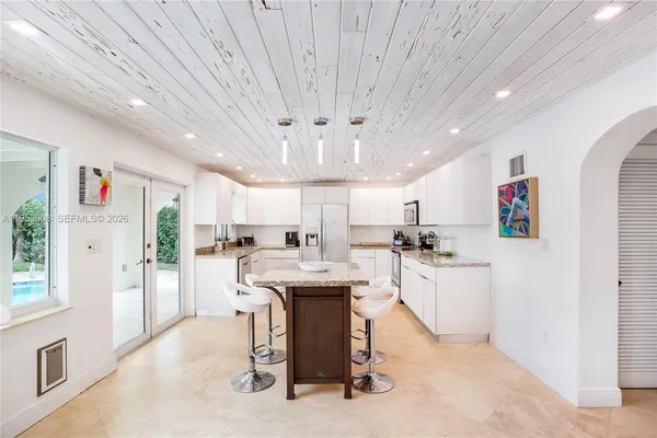 a kitchen with stainless steel appliances kitchen island granite countertop a refrigerator a sink dishwasher a dining table and chairs with wooden floor