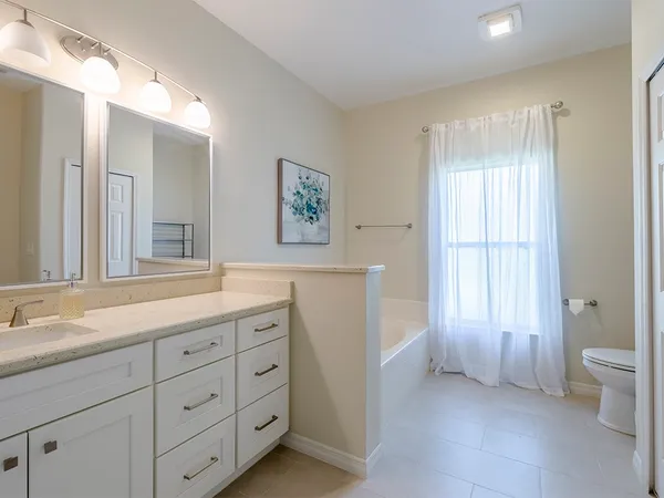 a spacious bathroom with a double vanity sink a large mirror a toilet and a window