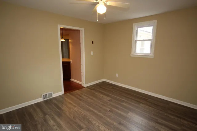 an empty room with wooden floor chandelier fan and windows