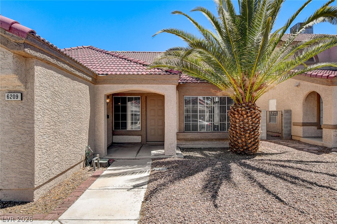 6209 Warm River Road Las Vegas, NV 89108 - Photo 4 of 39 A terracotta-tiled roof crowns this stucco residence, featuring a welcoming palm tree and a practical rock garden.