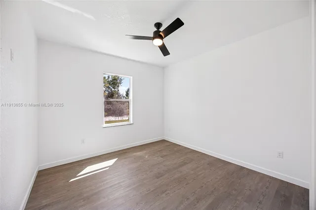 an empty room with wooden floor ceiling fan and window