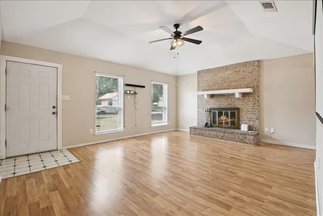 an empty room with wooden floor fireplace and windows